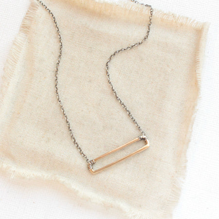 The bronze open bar with silver chain necklace styled on tan linen
