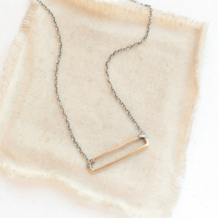 The bronze open bar with silver chain necklace styled on tan linen