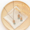The bronze wanderer arch green apatite necklace styled on a tan plate with the matching earrings