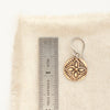 A bronze wanderer coin earring next to a ruler for size reference