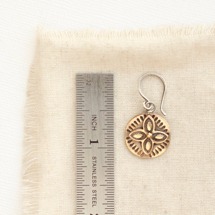 A bronze wanderer coin earring next to a ruler for size reference