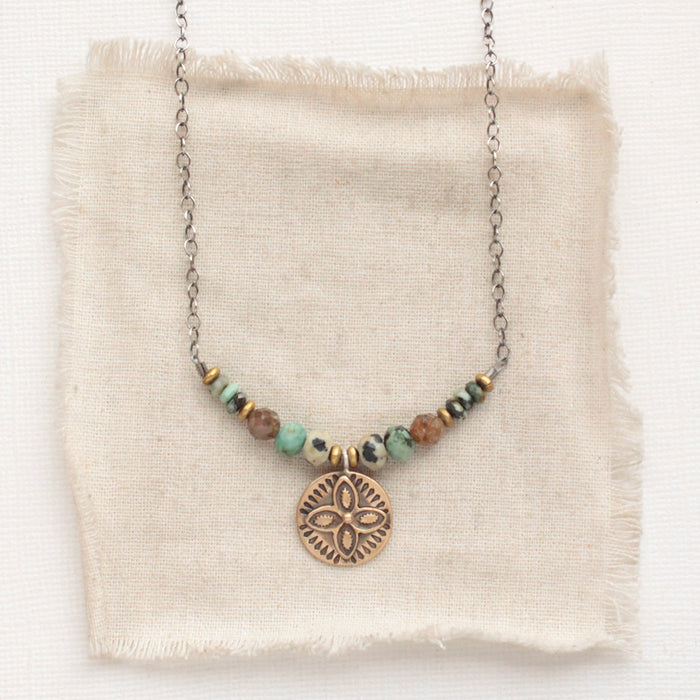 The bronze wanderer coin lona necklace styled on tan linen
