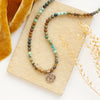 The bronze wanderer coin turquoise ombre necklace styled on a tan rock with yellow velvet and dried grass