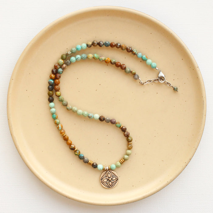 The bronze wanderer coin turquoise ombre necklace styled on a tan plate to show the adjustable lobster clasp closure