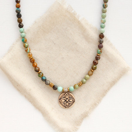 The bronze wanderer coin turquoise ombre necklace styled on tan linen