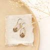 The bronze wanderer hoop earrings styled on a tan plate with linen and dried grass
