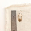 A bronze wanderer hoop earring next to a ruler for size reference