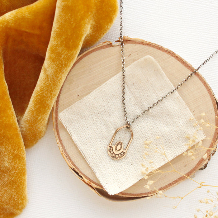 The bronze wanderer hoop necklace styled on wood with yellow velvet and dried grass