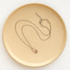 The bronze wanderer hoop necklace styled on a tan plate to show the adjustable lobster clasp closure