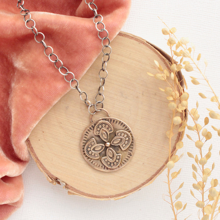 The bronze wanderer medallion necklace styled on wood with coral velvet and dried grass