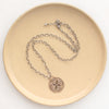 The bronze wanderer medallion necklace styled on a tan plate to show the adjustable lobster clasp closure