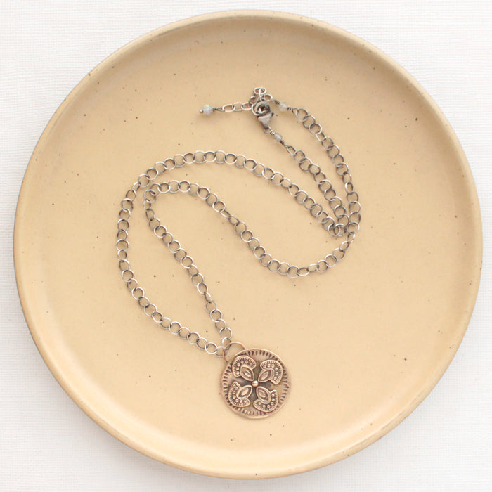 The bronze wanderer medallion necklace styled on a tan plate to show the adjustable lobster clasp closure