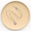 The brown zircon pakal arch necklace styled on a tan plate to show the adjustable lobster clasp closure