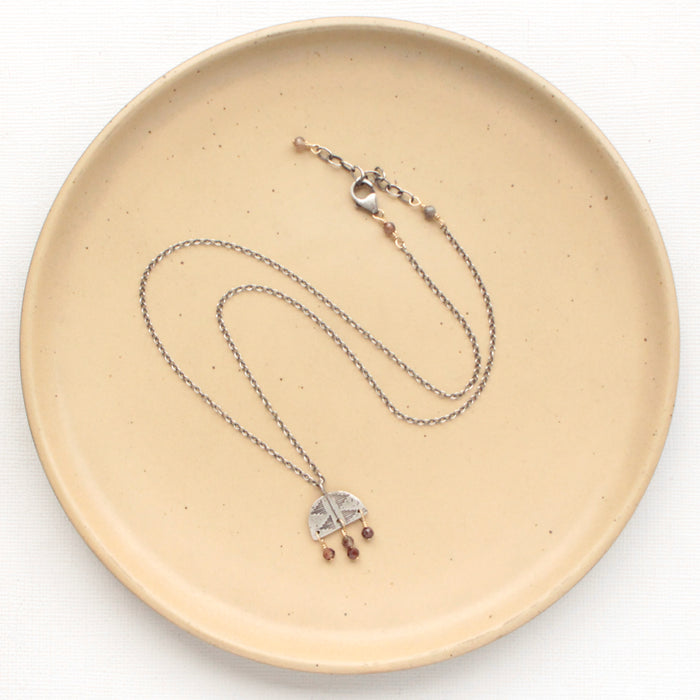 The brown zircon pakal arch necklace styled on a tan plate to show the adjustable lobster clasp closure
