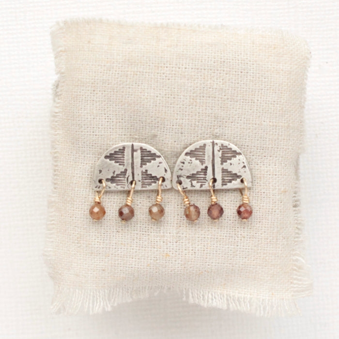 The brown zircon pakal arch post earrings styled on tan linen