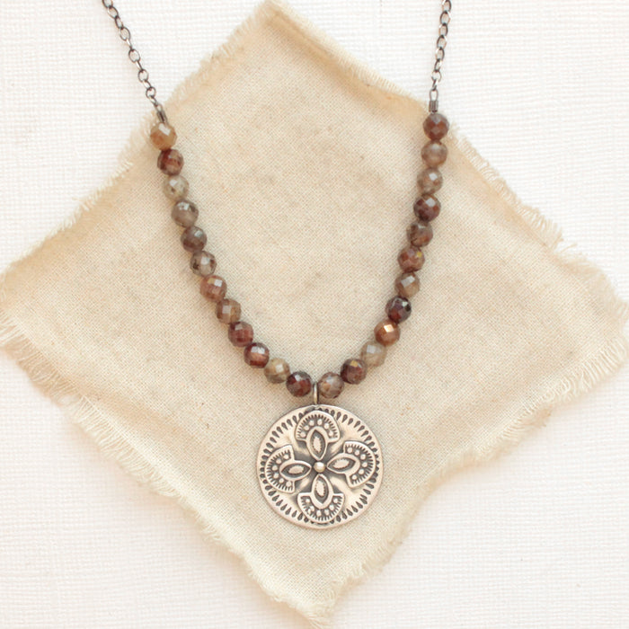 The brown zircon wanderer medallion necklace styled on tan linen