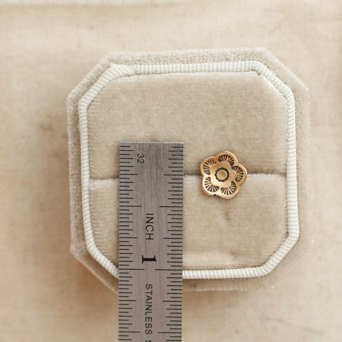 A bronze mini cactus flower post earring next to a ruler for size reference