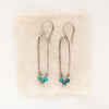 The chrysocolla forged long hoop earrings styled on tan linen.