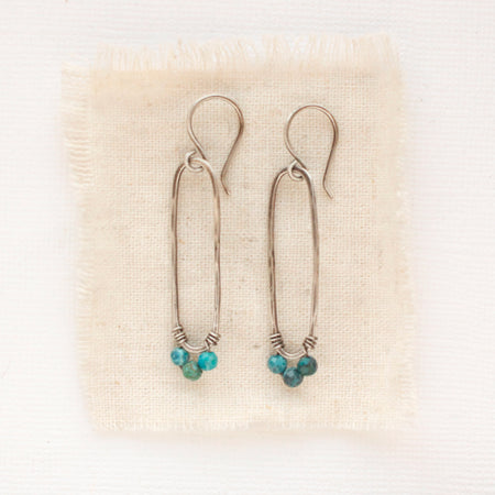 The chrysocolla forged long hoop earrings styled on tan linen.
