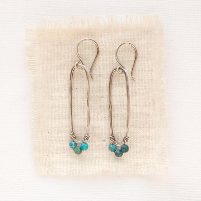 The chrysocolla forged long hoop earrings styled on tan linen.