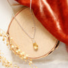 The citrine drop silver necklace styled on wood with orange velvet and dried grass