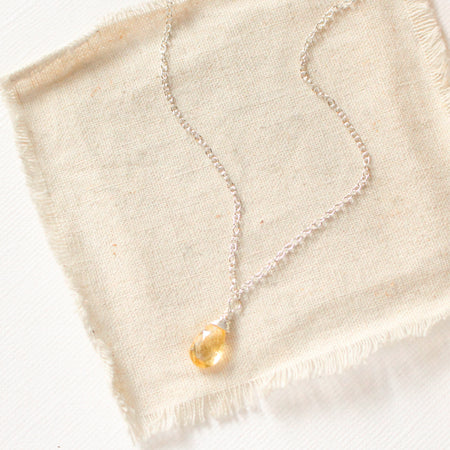 The citrine drop silver necklace styled on tan linen