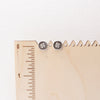 The stamped silver clover post earrings on a wooden ruler for size reference