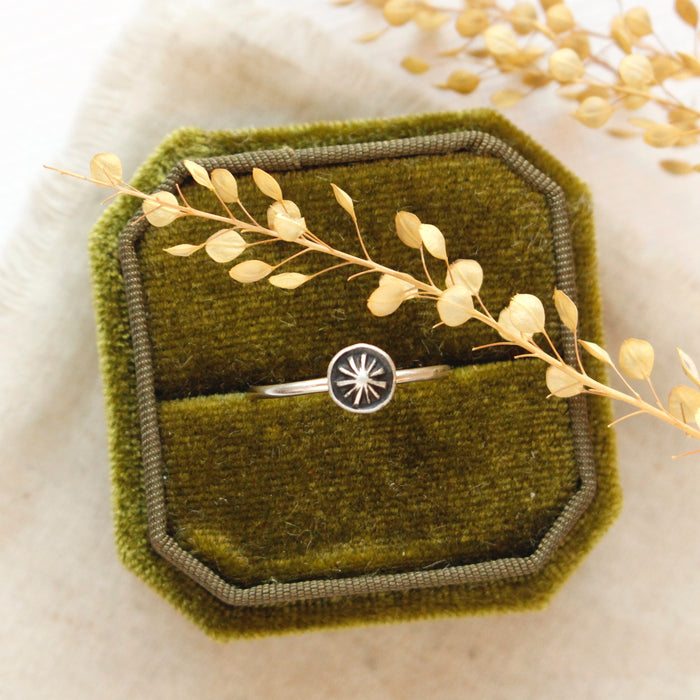 The columbine burst stacking ring styled on a green velvet box with linen and dried grass