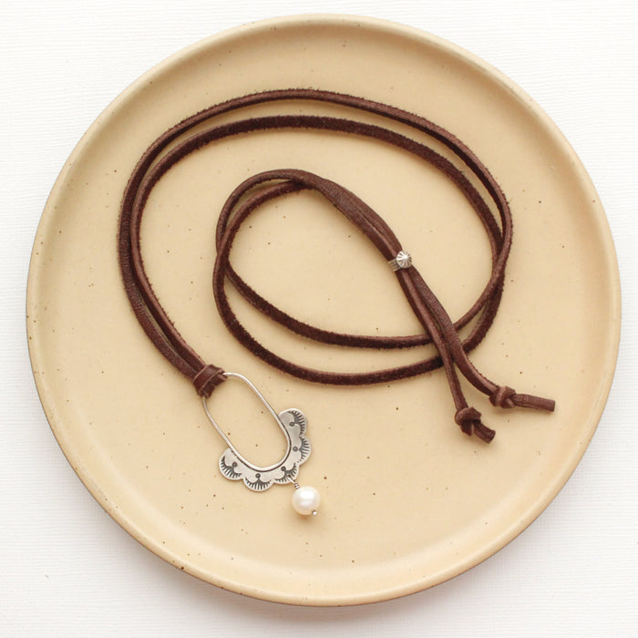 The columbine hoop pearl adjustable leather necklace styled on a tan plate to show the entire leather strap and silver slider