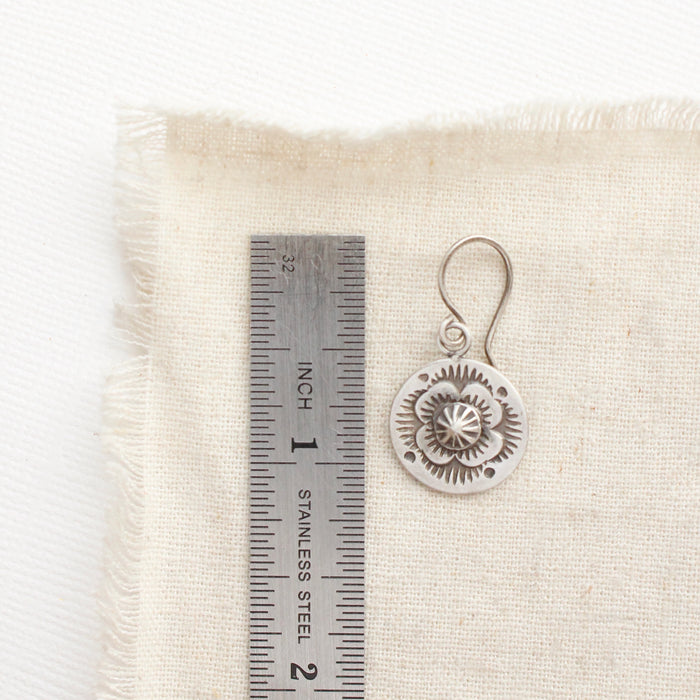 A columbine medallion earring next to a ruler for size reference