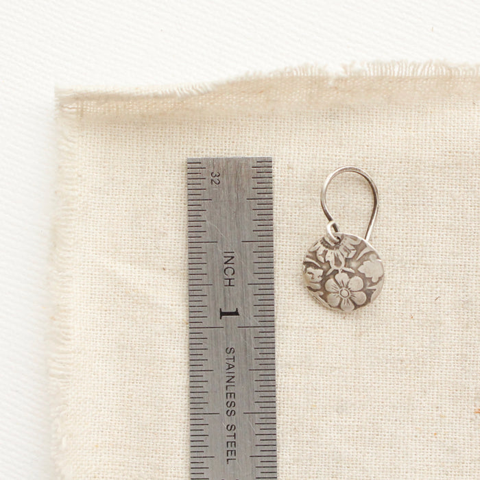 An embossed siena disc earring next to a ruler for size reference