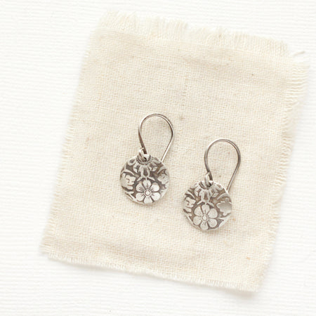 The embossed silver disc earrings styled on tan linen
