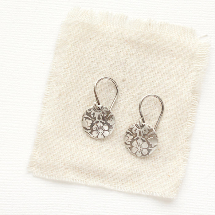 The embossed silver disc earrings styled on tan linen