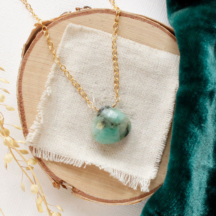 The emerald drop gold necklace styled on wood with green velvet and dried grass