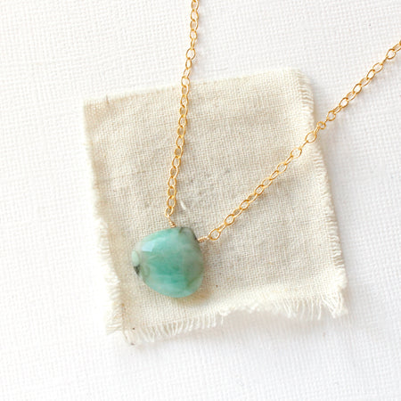 The emerald drop gold necklace styled on tan linen