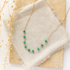 The emerald collar necklace styled on a tan rock with linen and dried grass