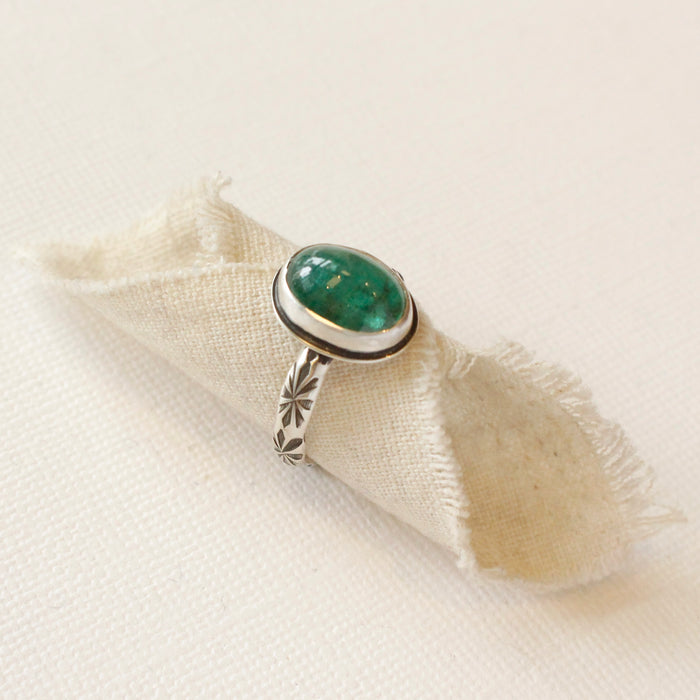 The emerald ring styled on tan linen to show the stamped silver band