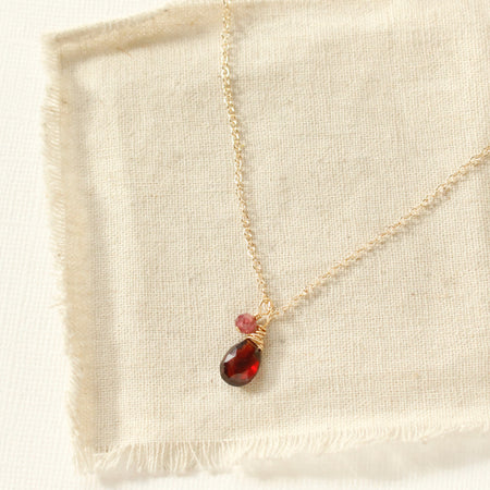 The garnet charm necklace styled on tan linen