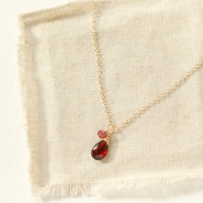 The garnet charm necklace styled on tan linen