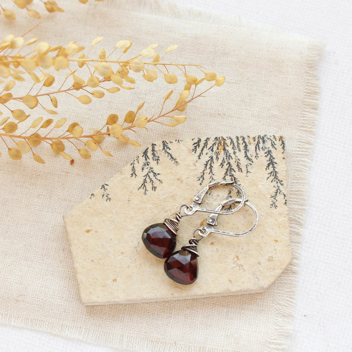The garnet drop earrings styled on a tan rock with linen and dried grass