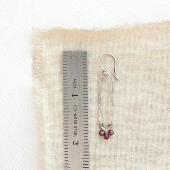 A garnet wrapped long forged hoop earring styled next to a ruler for size reference