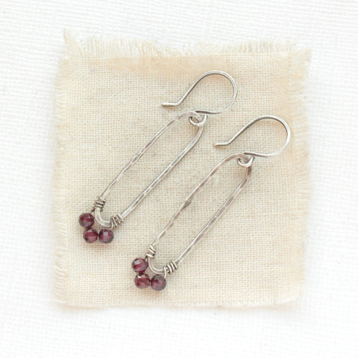 The garnet wrapped forged long hoop earrings styled on tan linen