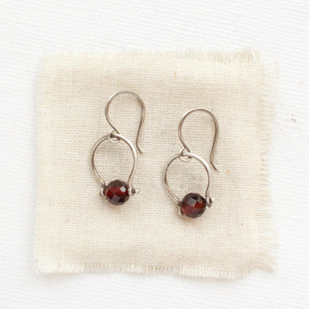 The garnet la cloche earrings styled on tan linen