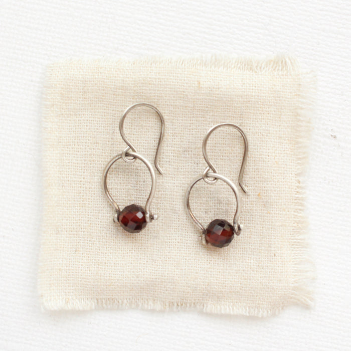 The garnet la cloche earrings styled on tan linen