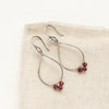 The garnet wrapped teardrop hoop earrings styled on tan linen