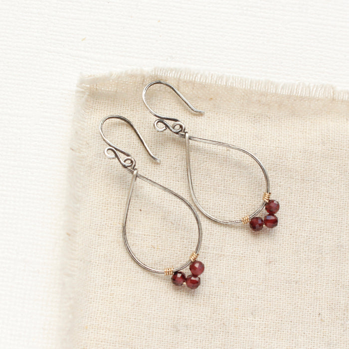 The garnet wrapped teardrop hoop earrings styled on tan linen