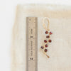 A garnet wrapped gold vine earring next to a ruler for size reference