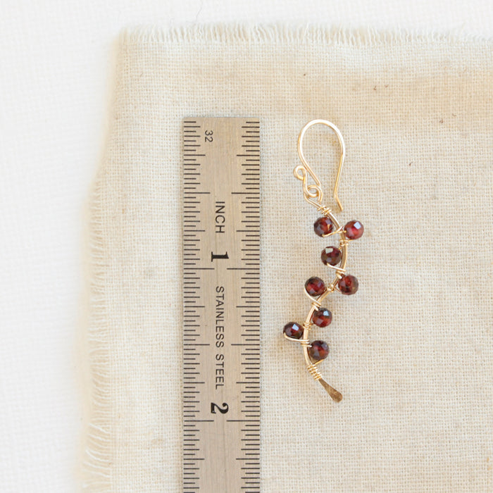 A garnet wrapped gold vine earring next to a ruler for size reference