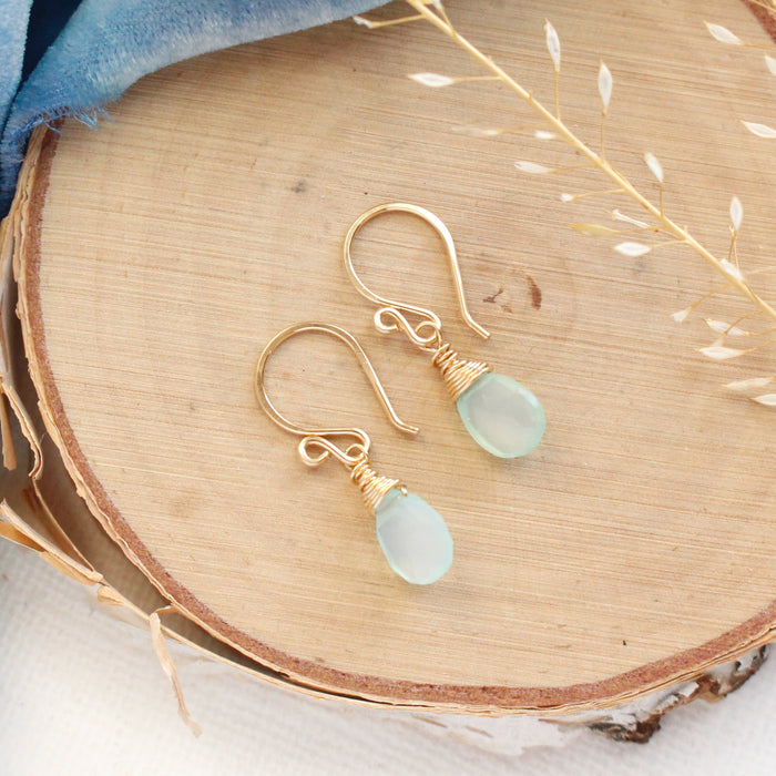 The gold chalcedony drop earrings styled on wood with blue velvet and dried grass