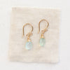 The gold chalcedony drop earrings styled on tan linen